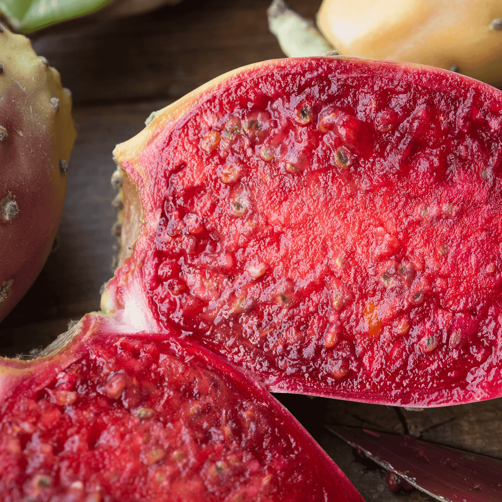 Be Bohemian Botanical Sea Serum Prickly Pear Seed Oil. Brilliantly juicy and red prickly pear split in half, shows different shades of red, ranging from blood red to bright red, with seeds poking through.