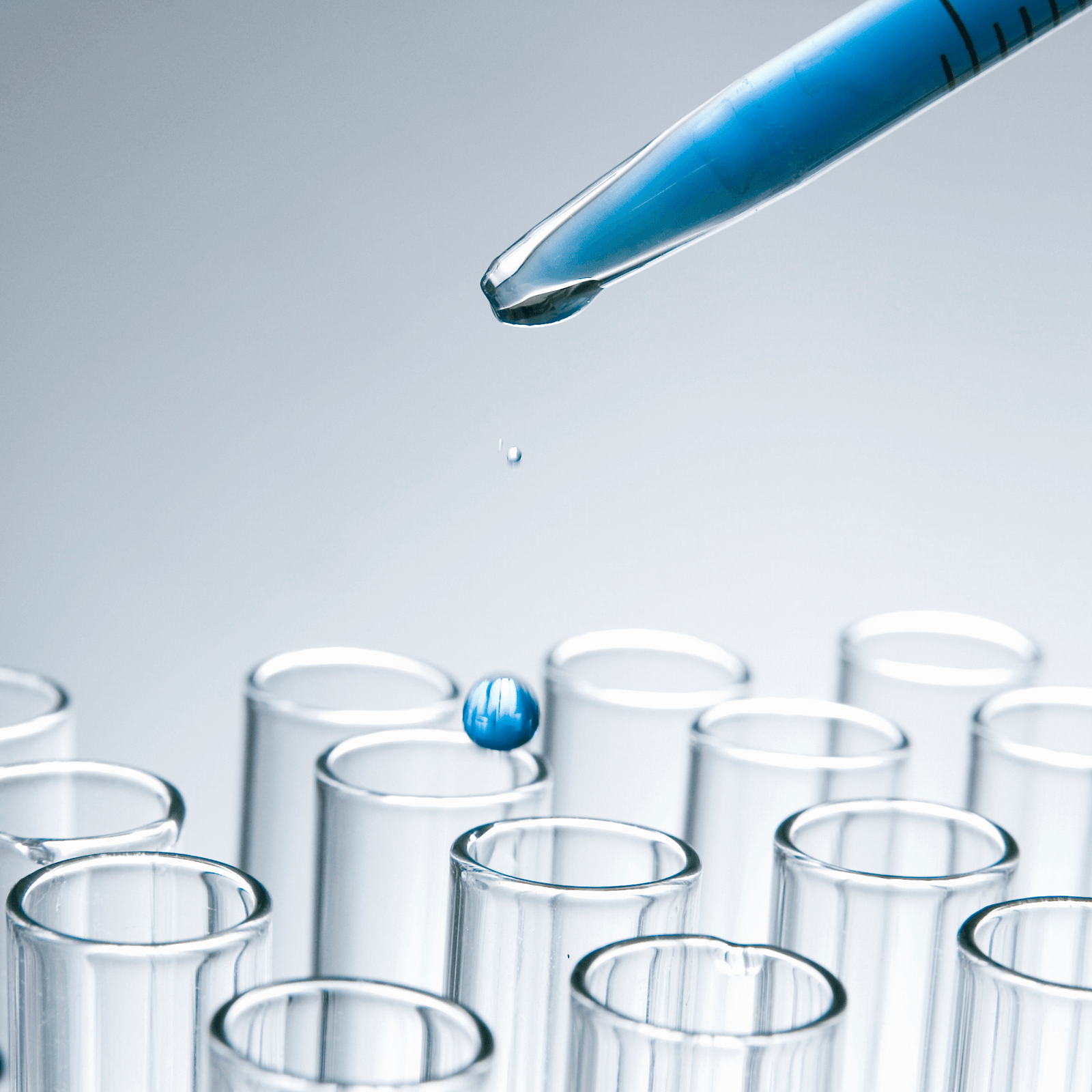 Be Bohemian Botanical Sea Serum lab made and naturally occurring in the body ingredients. A little blue drop of liquid is falling from the tip of a syringe filled with blue liquid over rows of clean lab beakers.