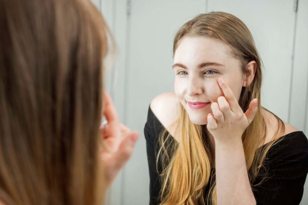 A woman applying Be Bohemian Botanical Sea Serum to her face in front of a mirror.
